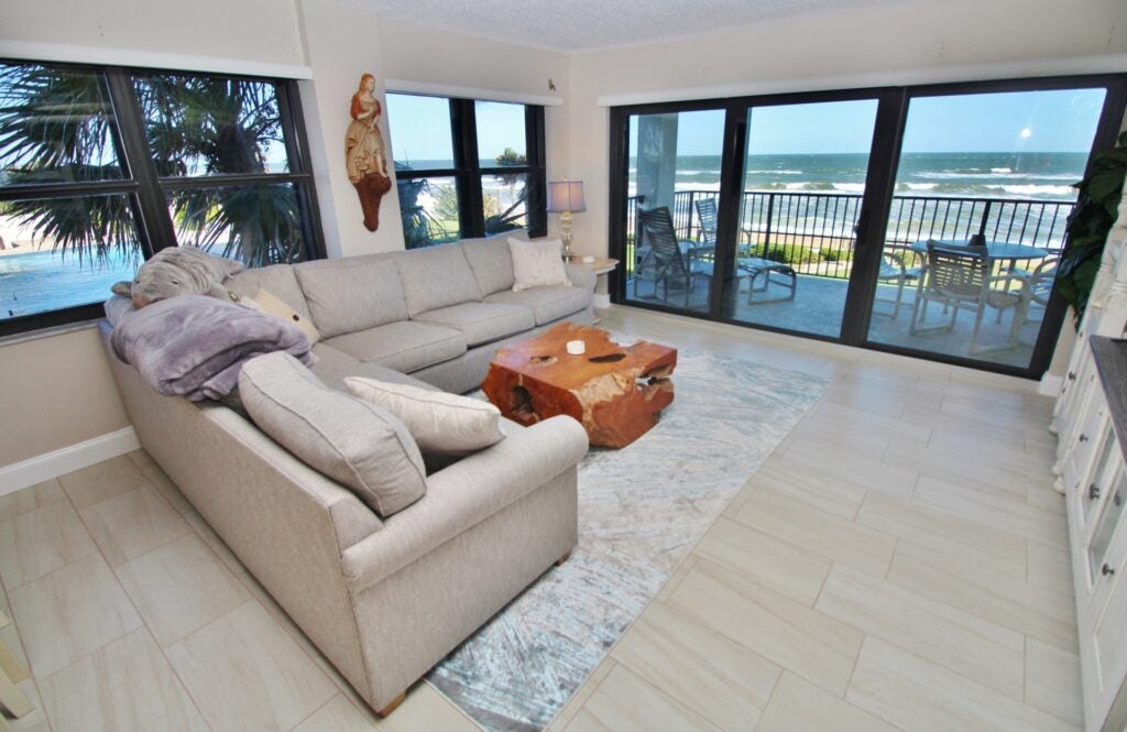 bright condo living room with large gray sectional and huge windows with ocean view.