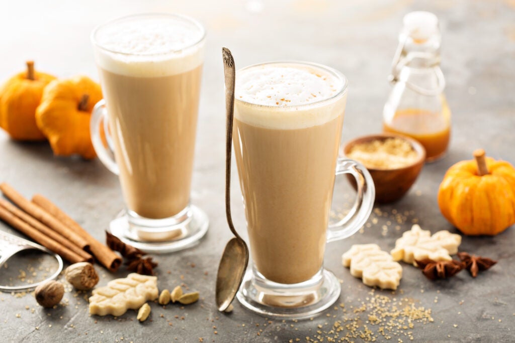 Two iced pumpkin spice lattes on a table with ingredients and pumpkins decorated around them