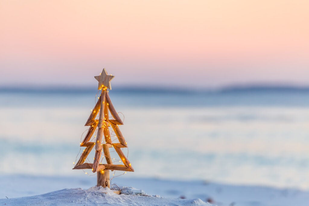 close up of small wooden Christmas tree in sand at beach with sun rise in background